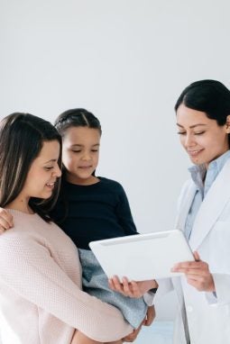 A latin female doctor holding a digital tablet and showing it to a girl patient and her mother.